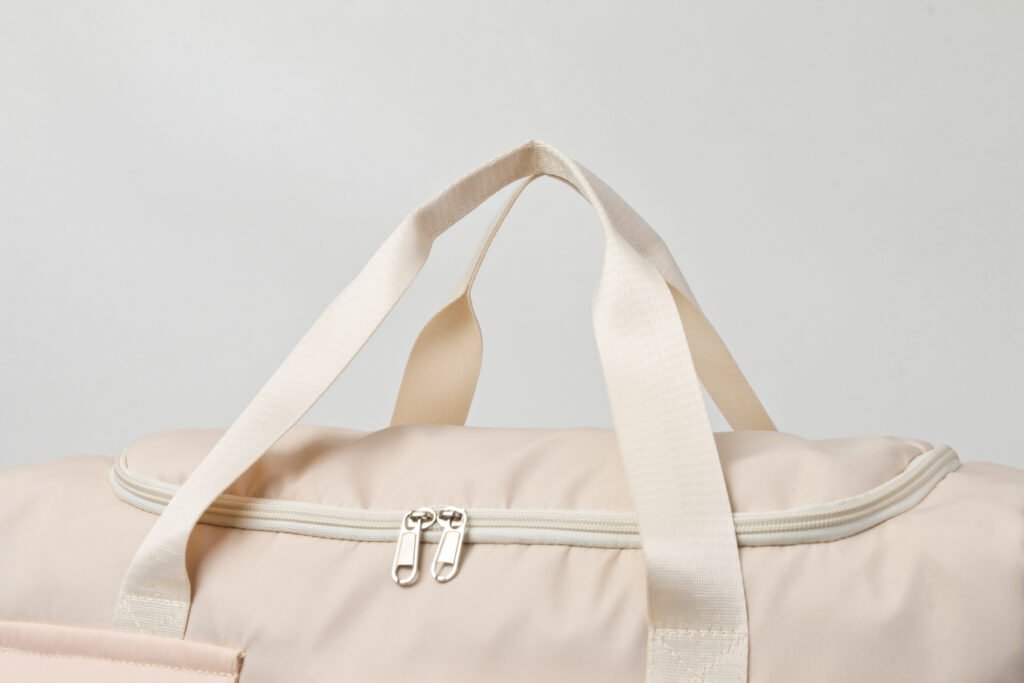 Close-up of the zipper and handles on a beige travel duffel bag