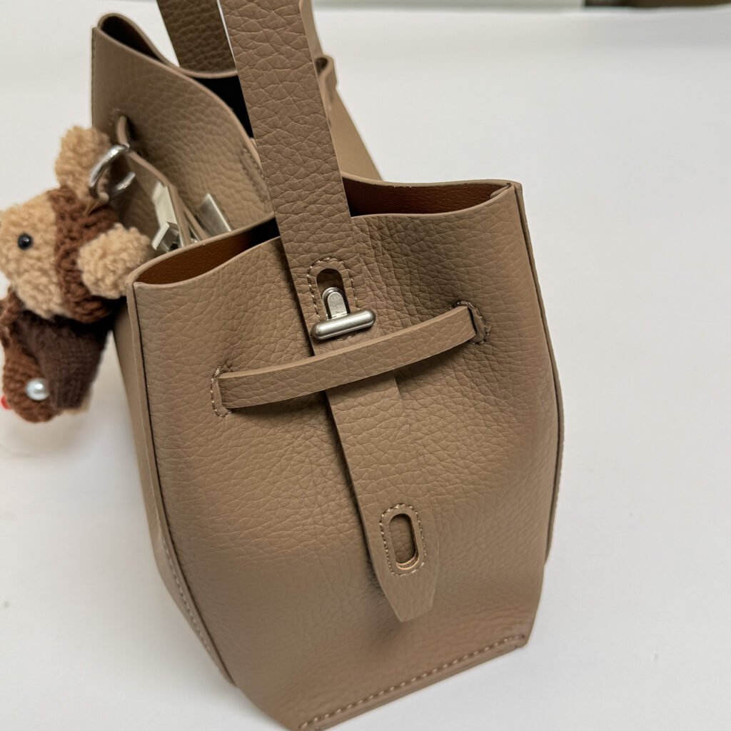 Side view of a taupe bucket bag and strap attachment