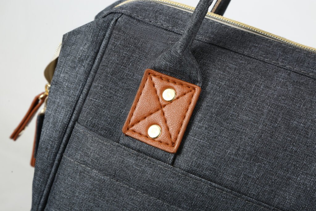 Backpack top handle attachment with stitched reinforcement patch and rivets