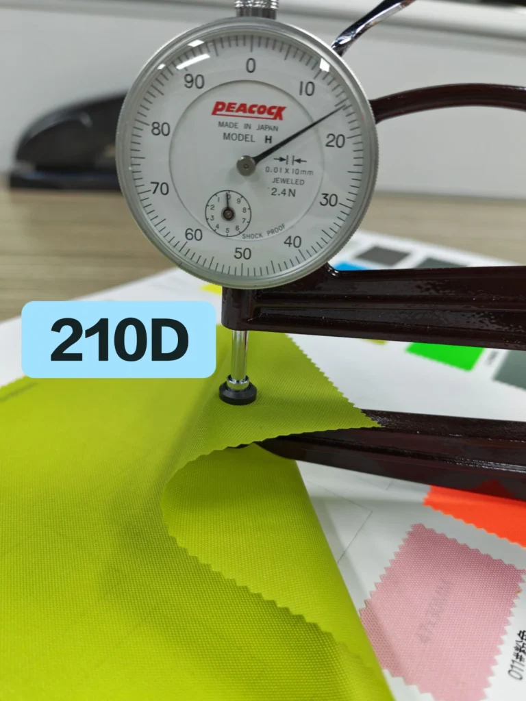 Thickness gauge contacting a green fabric swatch labelled 210D