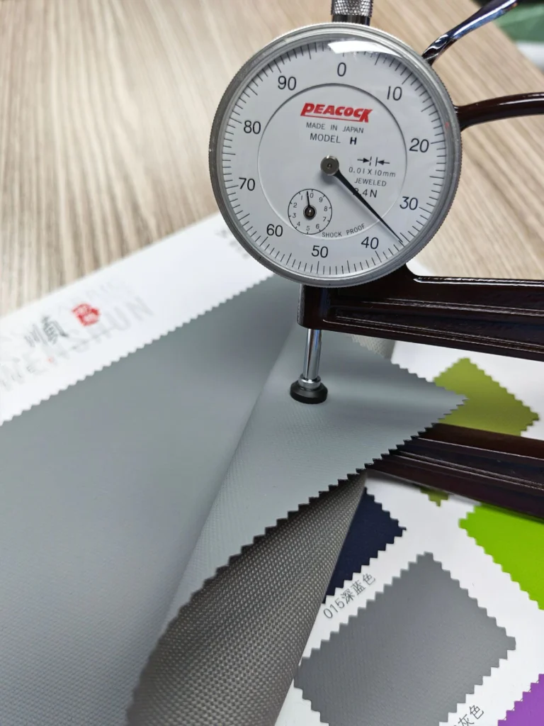 Dial thickness gauge contacting a grey fabric swatch